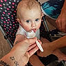 adult, baby, blue_eyes, child, clothing, curious, expression, feeding, floor, footwear, fork, hand, indoor, person, polka_dot, seat, skin, stroller, tattoo, toy