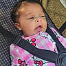 baby, child, car_seat, straps, pink_clothing, hello_kitty, face, curly_hair, infant, cute, safety, patterned_clothing, seatbelt, portrait, young_child, indoor, soft_light, expression, closeup, casual