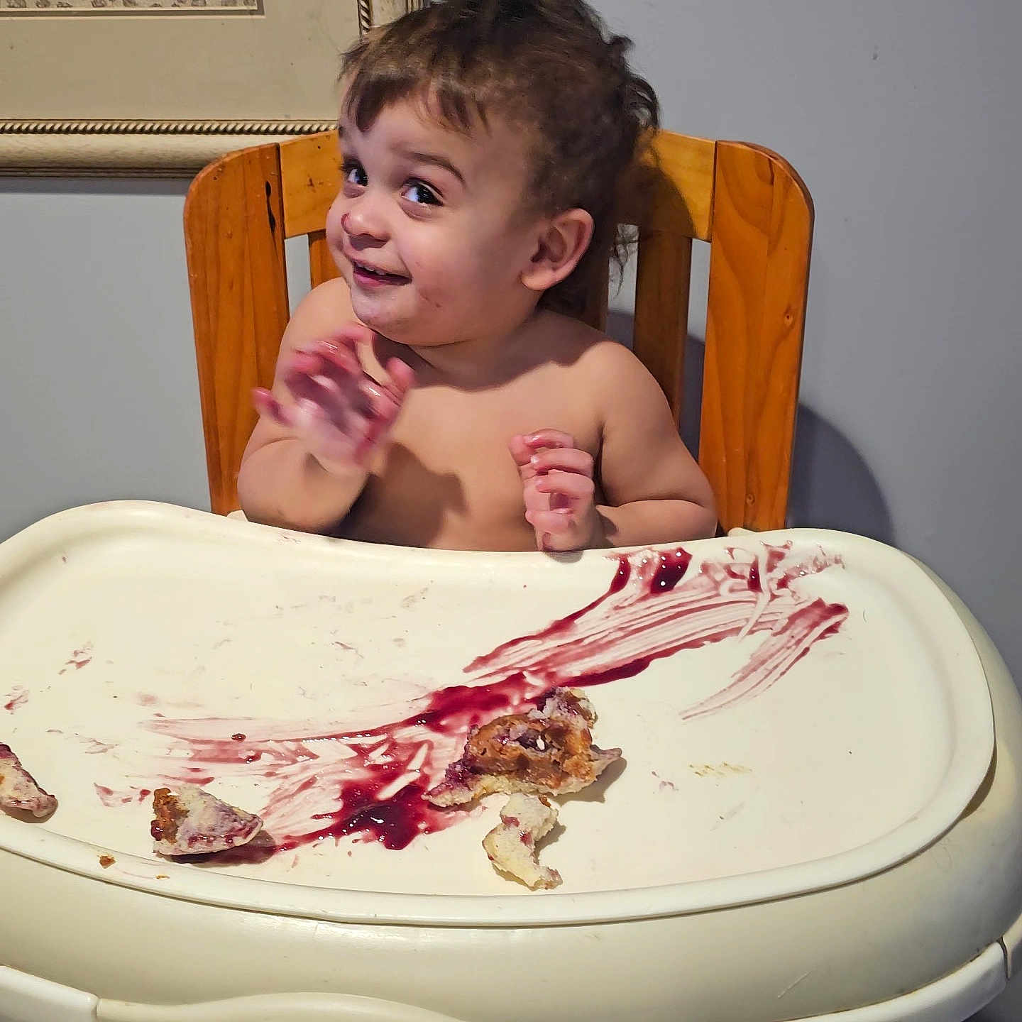 Kyler is registered to the contest to win money with this photo: toddler, child, high_chair, food, jam, crumbs, messy, smile, wooden_chair, face, hands, indoor, wall, tray, mess, happy, eating, portrait, cute, baby