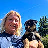 Sophia joined the competition — help win amazing prizes! woman, puppy, dog, smile, outdoor, blue_sky, greenery, sunlight, happy, portrait, holding, casual_clothing, short_hair, nature, tree, animal, pet, face, daytime, volunteer
