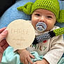 Marius participe au concours pour gagner de l'argent avec cette photo : baby, pacifier, knitted_hat, green_hat, blue_blanket, soft_blanket, milestone_marker, hand, cute, smiling, infant, portrait, closeup, cozy, child, clothing, indoor, face, person, holding