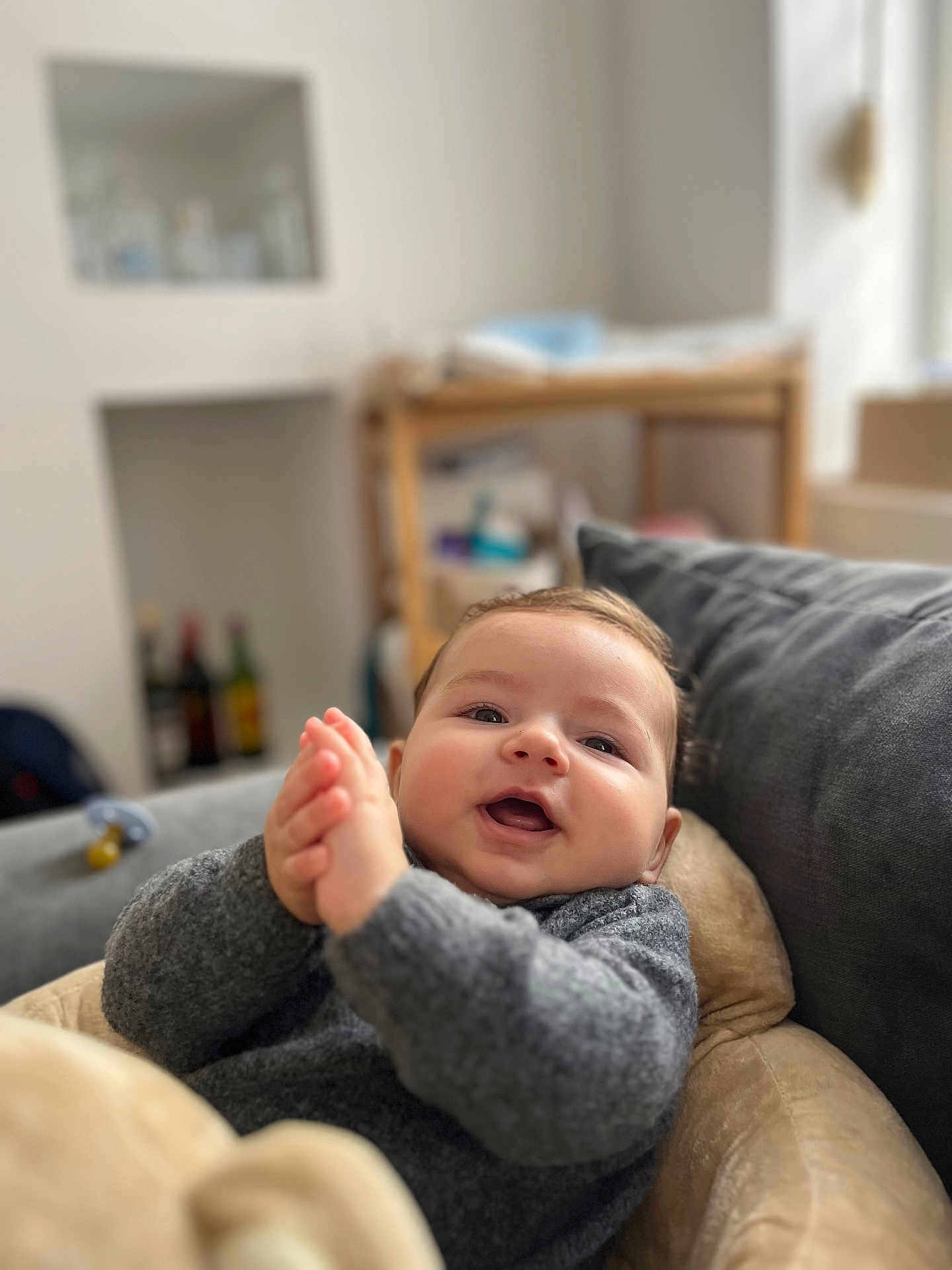 Marius a rejoint le concours — aidez-le/la à gagner de superbes lots ! baby, child, smiling, clapping, gray_sweater, cushion, indoors, home, cozy, happy, face, infant, person, portrait, soft_light, furniture, blurred_background, warm, cute, relaxed