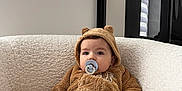 Marius participe au concours pour gagner de l'argent avec cette photo : baby, child, pacifier, fuzzy_outfit, bear_ears, plush_chair, indoor, window, modern_interior, white_wall, soft_texture, cute, infant, sitting, cozy, calm, portrait, clothing, young, person