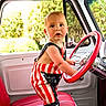 Levi joined the competition — help win amazing prizes! toddler, baby, child, car_interior, steering_wheel, red_seat, romper, american_flag_pattern, barefoot, window, daylight, greenery, vintage_car, curious_expression, indoor, portrait, person, seat, hand, face