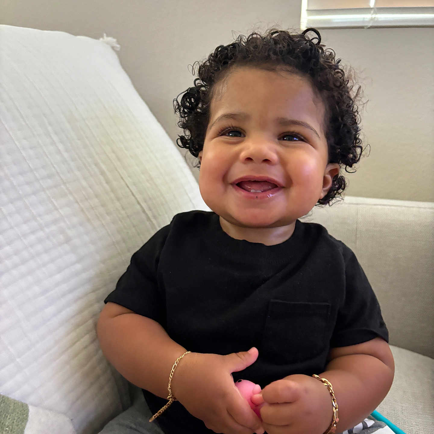Alonis Saint Patrick joined the competition — help win amazing prizes! baby, black_shirt, bracelet, child, couch, curly_hair, cute, gray_shorts, happy, home, indoor, light, person, portrait, sitting, skin, smiling, toddler, toy, window