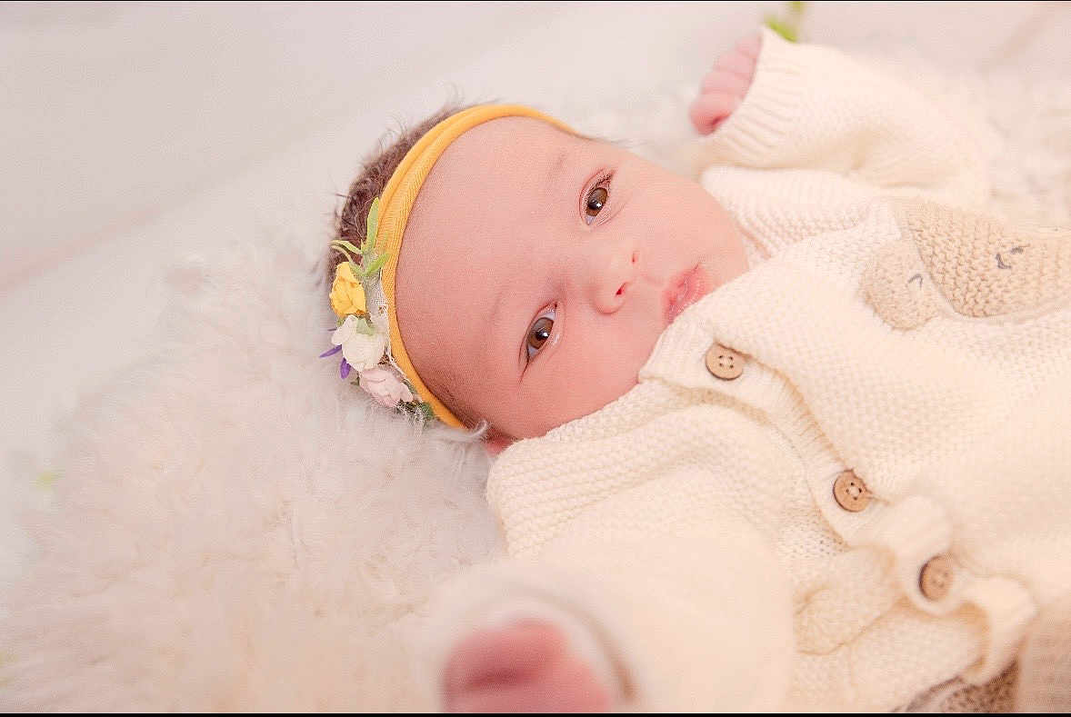 Jade participe au concours pour gagner de l'argent avec cette photo : baby, newborn, infant, headband, flower_headband, blanket, knit_sweater, buttons, soft_texture, portrait, close_up, eyes, cheeks, hand, lying_down, cozy, plush, fur_rug, sleepy, skin