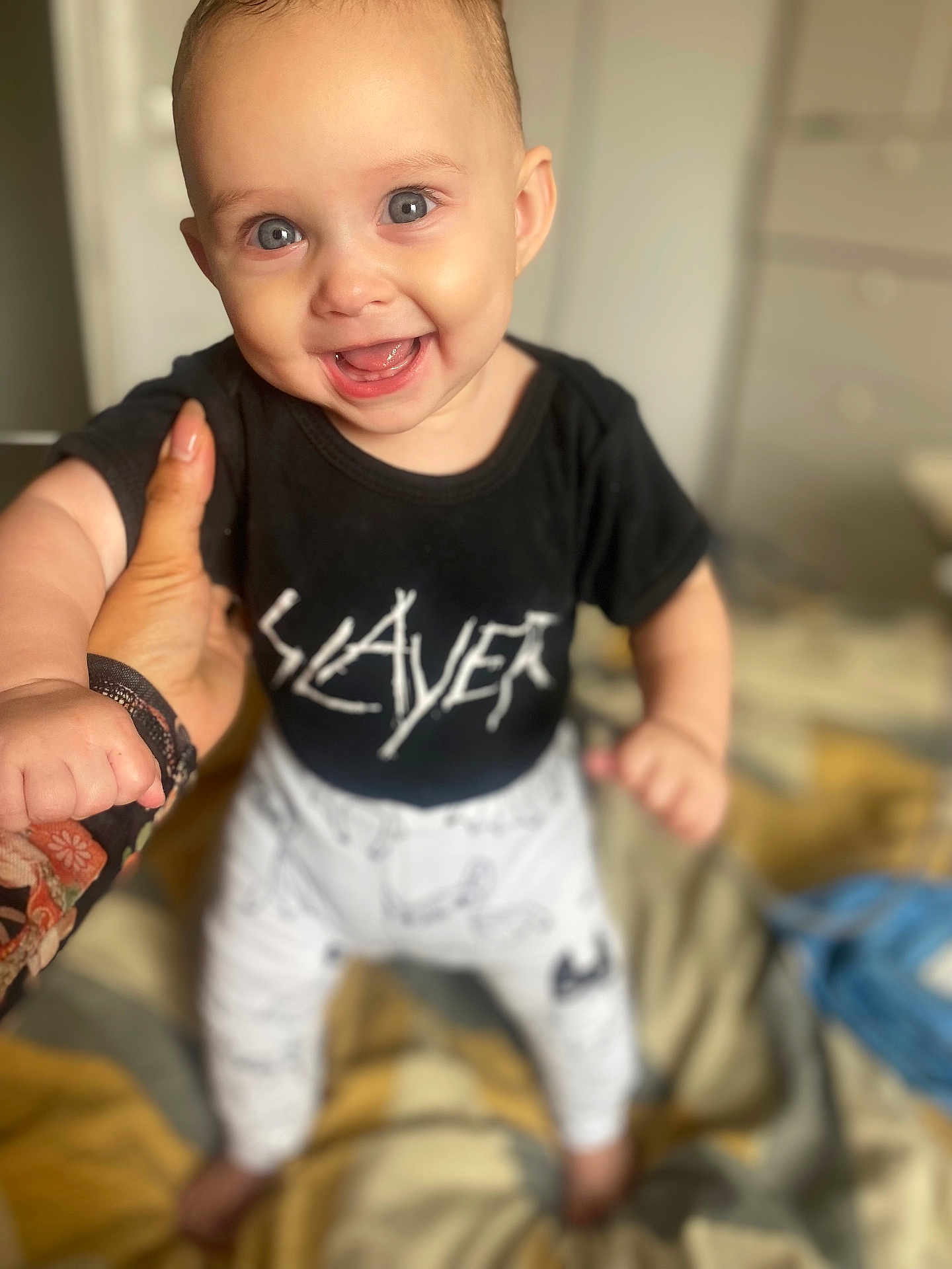 Aali joined the competition — help win amazing prizes! baby, child, smiling, blue_eyes, black_shirt, white_pants, hand, bed, indoor, person, happy, cute, standing, support, clothing, infant, face, portrait, human, background_blur