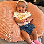 Esme is registered to the contest to win money with this photo: baby, infant, girl, smiling, headband, pink_socks, denim_shorts, cushion, knit, comfortable, happy, cute, clothing, indoor, person, child, portrait, resting, soft, expression