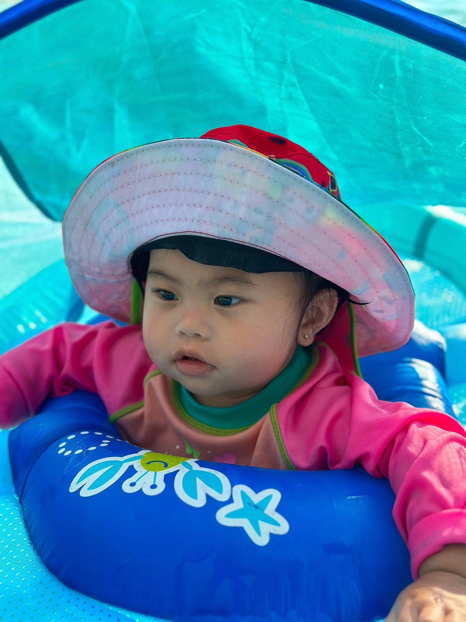 Flora is registered to the contest to win money with this photo: azure, baby, baby_toddler_clothing, blue, cap, cool, eye, grass, green, happy, hat, headgear, headwear, leisure, person, photograph, pink, recreation, skin, sun_hat