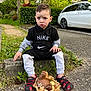 toddler, child, outdoor, sitting, concrete_block, chocolate, basket, hen, eggs, nike, hoodie, shoes, grass, car, tree, sidewalk, expression, clothing, person, nature