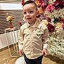 child, boy, flower_wall, balloon, striped_shirt, pants, indoor, wooden_floor, decor, vase, flowers, curious_expression, standing, casual_clothing, young, portrait, celebration, decorative, plant, event
