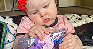 Bonnie is registered to the contest to win money with this photo: baby, blanket, carpet, child, colorful, cozy, curious, face, focus, hair_clip, hands, indoor, living_room, person, pink_shirt, red_bow, sitting, toddler, toy, young_child