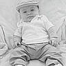baby, child, infant, cap, shirt, pants, sneakers, footwear, blanket, seated, portrait, monochrome, black_and_white, cute, fashion, serious_expression, indoor, soft_texture, comfortable, young