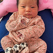 Aurora is registered to the contest to win money with this photo: newborn, baby, infant, onesie, pink, floral_pattern, toy, soccer_balls, cushion, pillow, indoor, person, face, head, clothing, sleepwear, cute, resting, child, small
