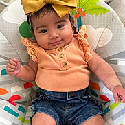 Aurelia is registered to the contest to win money with this photo: baby, child, infant, smiling, headband, bow, clothing, peach_top, denim_shorts, sitting, baby_seat, colorful, indoor, cute, portrait, happy, young_child, person, closeup, comfortable