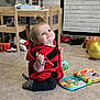Elise a rejoint le concours — aidez-le/la à gagner de superbes lots ! toddler, child, indoors, toy, balloon, red_hoodie, ladybug_pattern, floor, playtime, smiling, curious, wooden_furniture, colorful, cute, young_child, playroom, socks, hair_tie, educational_toy, happy