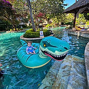Elise a rejoint le concours — aidez-le/la à gagner de superbes lots ! toddler, child, inflatable, dinosaur, pool, water, swimming_pool, float, outdoor, summer, sunny, trees, greenery, vacation, relaxation, steps, resort, blue_sky, casual_clothing, playful