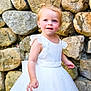 toddler, child, white_dress, stone_wall, outdoor, curly_hair, blue_eyes, cute, innocent, portrait, smiling, baby, fashion, dress, person, young_child, happy, summer, daylight, skin
