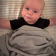 Noah joined the competition — help win amazing prizes! baby, infant, blanket, striped_sheet, lying_down, smiling, arms_outstretched, cozy, indoor, soft_lighting, cute, wrapped, child, person, face, head, skin, comfort, bed, resting