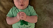Angelo is registered to the contest to win money with this photo: baby, infant, child, onesie, green_clothing, st_patricks_day, clasped_hands, lying_down, soft_blanket, indoor, cute, portrait, face, expression, young_child, skin, person, head, short_hair, celebration