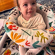 Angelo is registered to the contest to win money with this photo: baby, child, infant, smile, face, eyes, baby_chair, patterned_fabric, colorful, indoor, floor, wooden_floor, rug, clothing, sitting, comfort, cute, portrait, home, young