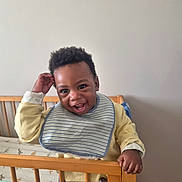 Caleb participe au concours pour gagner de l'argent avec cette photo : toddler, child, crib, smile, happy, indoor, clothing, bib, yellow_sweater, wooden_crib, playful, face, person, baby, standing, hand, hair, room, cute, expression