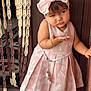 toddler, child, girl, pink_dress, headband, bow, bracelet, door, wooden_beads, curtain, floor_tiles, expression, posing, indoor, cute, fashion, accessory, standing, person, portrait