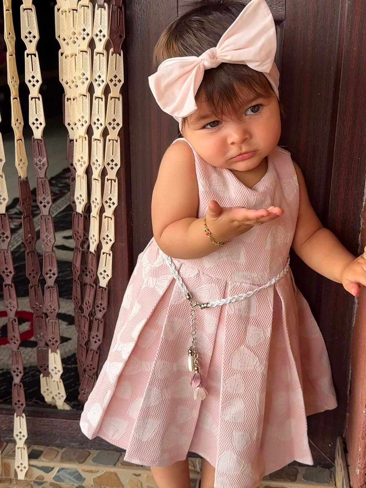 Moajer Azaleea a rejoint le concours — aidez-le/la à gagner de superbes lots ! toddler, child, girl, pink_dress, headband, bow, bracelet, door, wooden_beads, curtain, floor_tiles, expression, posing, indoor, cute, fashion, accessory, standing, person, portrait