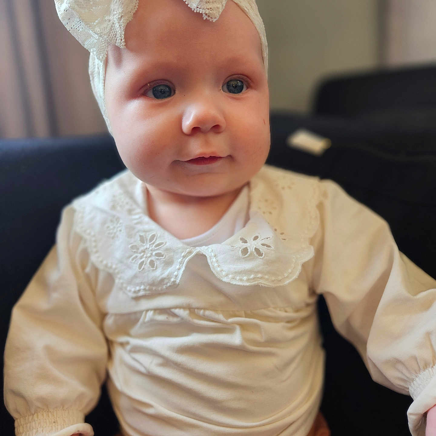 Mabel is registered to the contest to win money with this photo: accessories, baby, bodypart, bonnet, clothing, couch, dress, face, finger, hand, hat, head, headband, longsleeve, pants, person, photography, portrait, sitting, sleeve