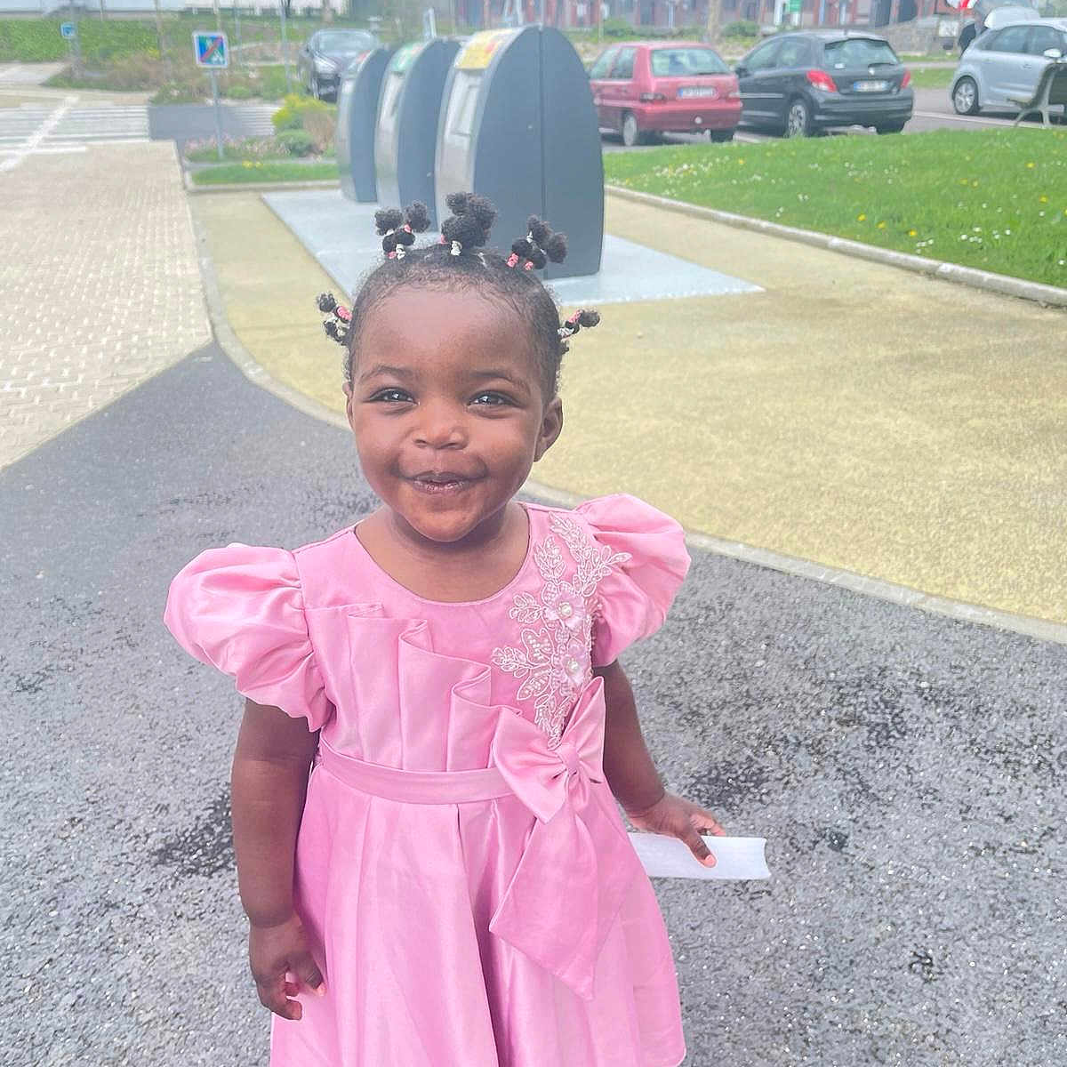 Joanna a rejoint le concours — aidez-le/la à gagner de superbes lots ! car, child, cute, daylight, fashion, footwear, grass, greenery, hair_puffs, happy, outdoor, parked_cars, pavement, person, pink_dress, playful, portrait, smile, toddler, young_child