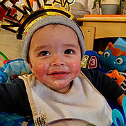 Axel joined the competition — help win amazing prizes! baby, child, smiling, hat, bib, happy_new_year, headband, indoor, toy, face, cheeks, clothing, person, infant, cute, celebration, home, furniture, plant, colorful