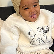 Lucas participe au concours pour gagner de l'argent avec cette photo : child, baby, toddler, face, smile, tongue_out, curly_hair, beanie, pompom_hat, sweater, lion_king, simba, patterned_pants, cozy, plush_texture, hand, seated, couch, indoors, happy