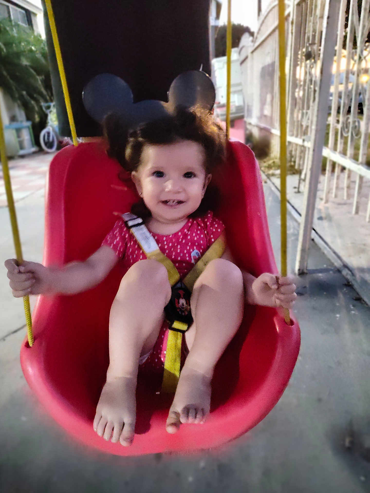 Isabel Escobedo is registered to the contest to win money with this photo: toddler, child, swing, red_swing_seat, yellow_straps, smiling, curly_hair, outdoor, playground, gate, concrete_floor, holding_rope, happy, person, baby, casual_clothing, daylight, play, fun, safety_harness
