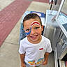 child, boy, face_paint, smile, outdoor, sidewalk, casual_clothing, shorts, white_tshirt, summer, happy, portrait, blue_eyes, short_hair, standing, colorful, footwear, concrete, fun, daytime