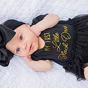 Naomi is registered to the contest to win money with this photo: baby, infant, black_dress, headband, bow, blanket, laying_down, cute, portrait, child, fashion, sparkle, white_background, clothing, newborn, soft_light, smiling, skin, baby_girl, closeup