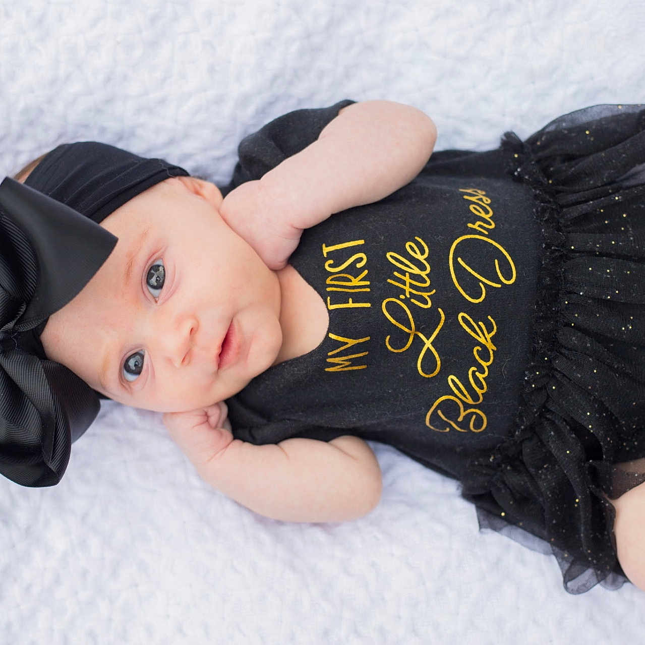 Naomi is registered to the contest to win money with this photo: baby, infant, black_dress, headband, bow, blanket, laying_down, cute, portrait, child, fashion, sparkle, white_background, clothing, newborn, soft_light, smiling, skin, baby_girl, closeup