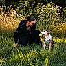 animal, casual_clothing, crouching, daylight, dog, field, grass, greenery, happy, interaction, leash, nature, outdoor, park, person, pet, playing, summer, sunlight, tennis_ball