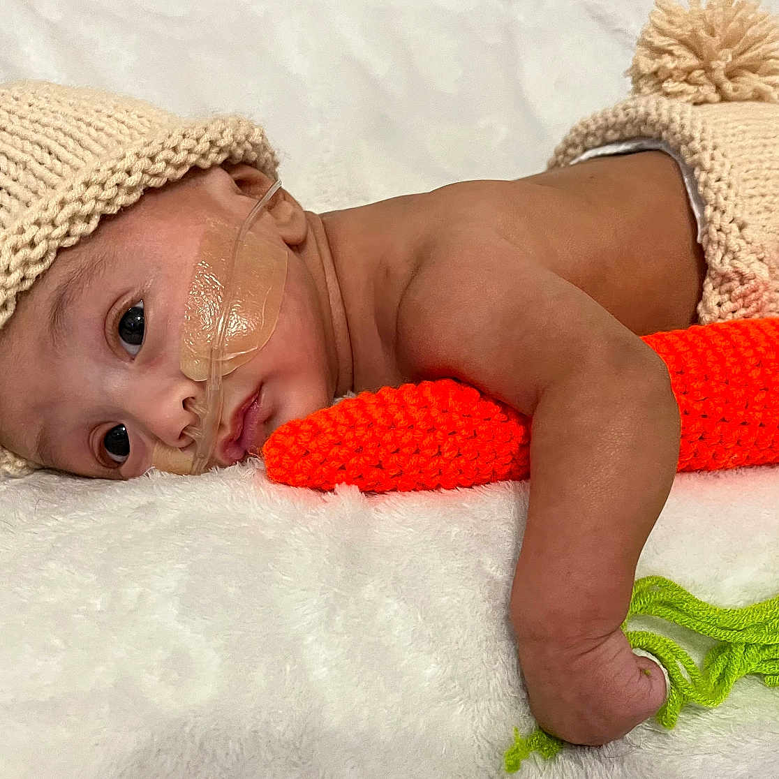 Elijah is registered to the contest to win money with this photo: architecture, baby, blanket, bodypart, bonnet, building, cap, clothing, crying, face, finger, hand, hat, head, hospital, newborn, person, photography, portrait, sad