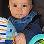 baby, denim_overalls, toy, blanket, clothing, child, infant, hand, face, eyes, portrait, cute, indoor, colorful, soft_toys, young_child, closeup, expression, holding, seated