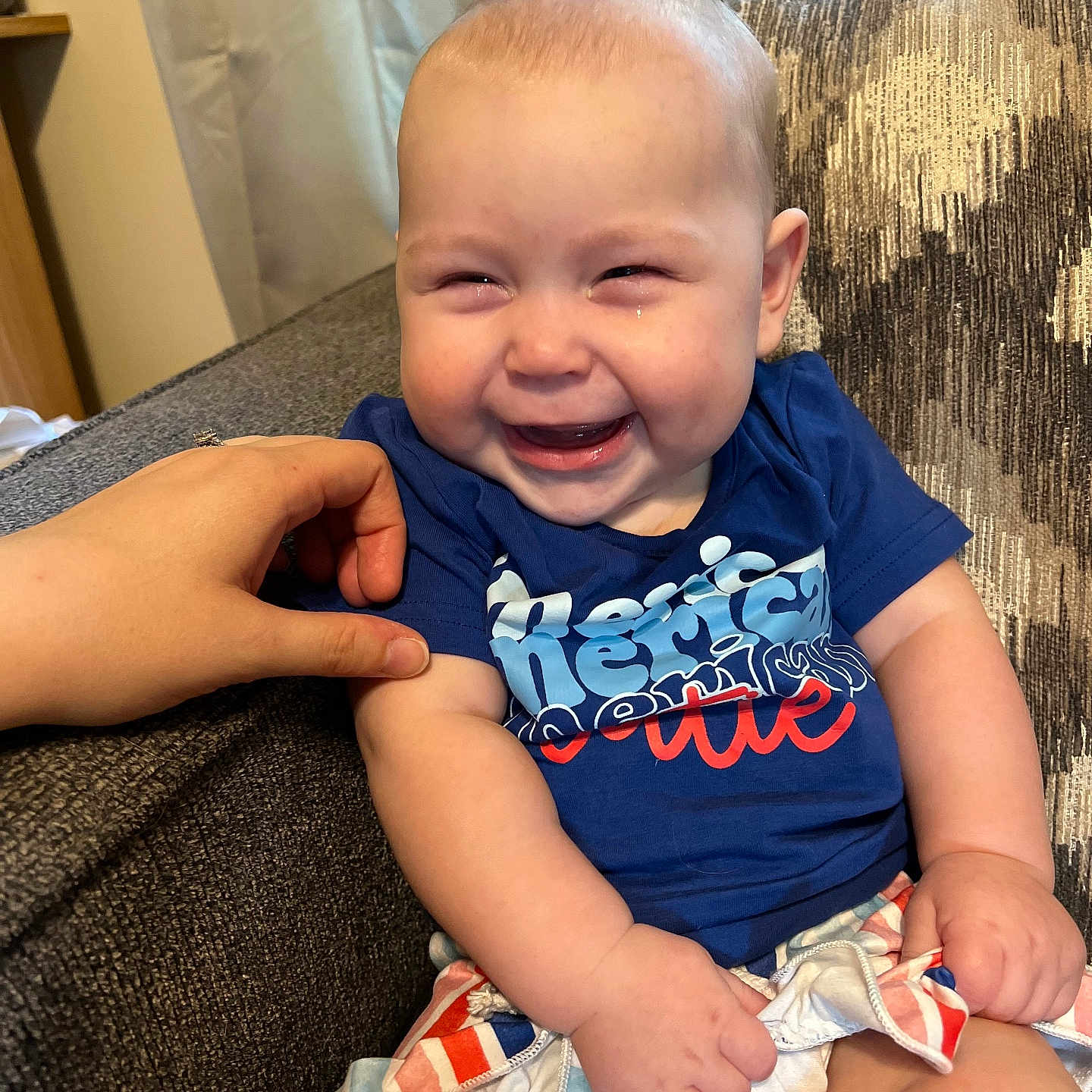 Sophia is registered to the contest to win money with this photo: baby, blue_shirt, child, chubby_arms, colorful_shorts, comfort, couch, curtain, cute, fabric, face, hand, happy, indoor, laughing, person, seated, skin, smiling, tickling
