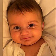 Yacob is registered to the contest to win money with this photo: baby, blanket, cheeks, child, closeup, cute, eyes, face, happy, head, indoors, infant, lying_down, portrait, skin, sleeping_area, smile, soft_lighting, white_clothing, young_child