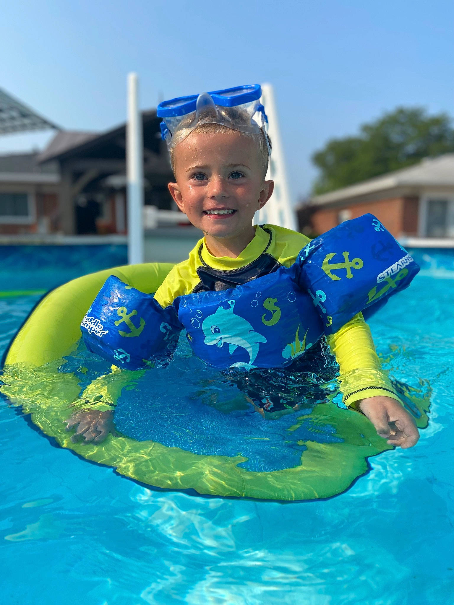 Carter is registered to the contest to win money with this photo: baby_toddler_clothing, blue, child, electric_blue, fun, happy, headgear, inflatable, joy, leisure, outdoor_recreation, person, personal_protective_equipment, recreation, sky, smile, sunglasses, swimming_pool, toddler, tree
