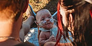 Braxton is registered to the contest to win money with this photo: baby, infant, nasal_tube, oxygen_tube, medical_tape, outdoor, grass, blanket, adult, holding, love, family, care, sunlight, warm_light, closeup, head, face, skin, person