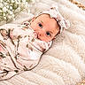baby, infant, wrapped, blanket, headband, flower_pattern, cushion, soft_texture, blue_eyes, portrait, cozy, resting, closeup, indoor, cute, newborn, floral, peaceful, baby_bedding, soft_lighting