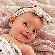 Esmae is registered to the contest to win money with this photo: baby, smiling, headband, bow, blanket, floral, cute, infant, skin, portrait, child, happy, texture, fabric, soft, lying_down, closeup, indoors, toddler, wrapped