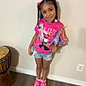 Khrystlyn is registered to the contest to win money with this photo: child, girl, smiling, portrait, standing, indoors, braids, hair_accessories, pink_shirt, graphic_shirt, denim_shorts, pink_shoes, unicorn_toy, hobby_horse, toy, drum, wood_floor, wall, electrical_outlet, fashion