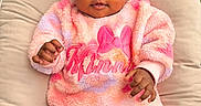 Peyton is registered to the contest to win money with this photo: baby, infant, child, pink_clothing, sweater, minnie, cushion, patterned_background, curly_hair, portrait, indoor, soft_texture, cozy, cute, smiling, hands, legs, comfortable, seated, closeup