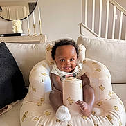 Peyton joined the competition — help win amazing prizes! baby, infant, smile, couch, living_room, inflatable_chair, bear_pattern, curly_hair, white_clothing, socks, decor, mirror, candles, stairs, home_interior, cute, seated, child, cozy, happy
