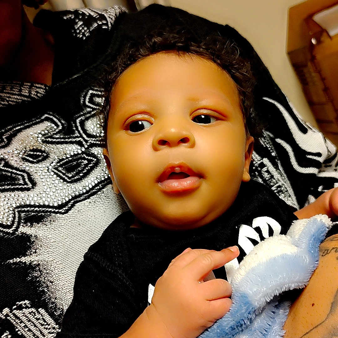 Ka'Marion joined the competition — help win amazing prizes! baby, child, blanket, black_clothing, indoor, person, arm, tattoo, heart_graphics, soft_texture, curly_hair, cute, holding, closeup, portrait, skin, furniture, fabric, comfort, warmth