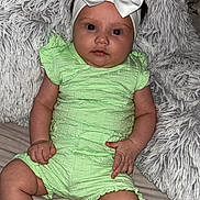 Ariella joined the competition — help win amazing prizes! baby, infant, child, green_outfit, headband, white_bow, red_eye, fluffy_blanket, soft_texture, sitting, indoors, cute, portrait, hands, legs, skin, face, expression, clothing, comfort